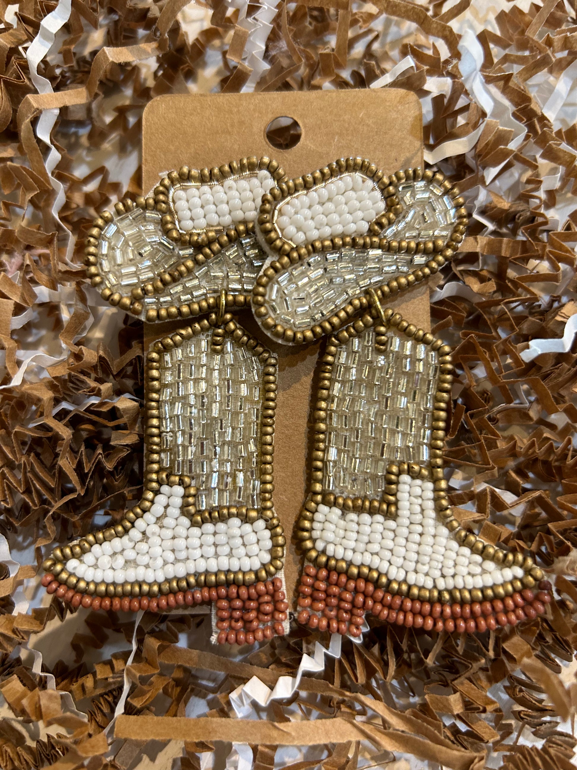 Beaded dangling earrings in the shape of cowboy hats and boots with gold and white beads.