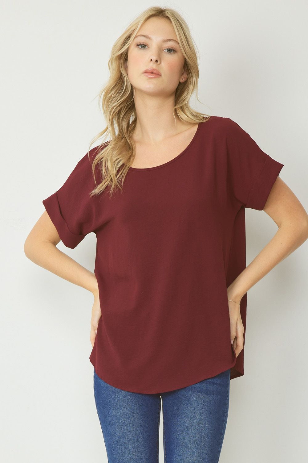 Burgundy scoop-neck top featuring permanent rolled sleeve detail and an asymmetrical hem.
