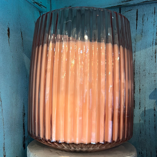 Candle in a rosy-hued, ripple textured jar.