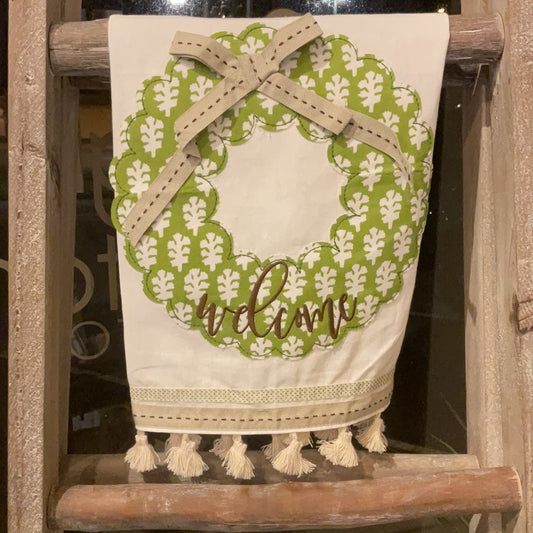 Off-white towel with tassels featuring a green wreath with a tan bow and "Welcome".