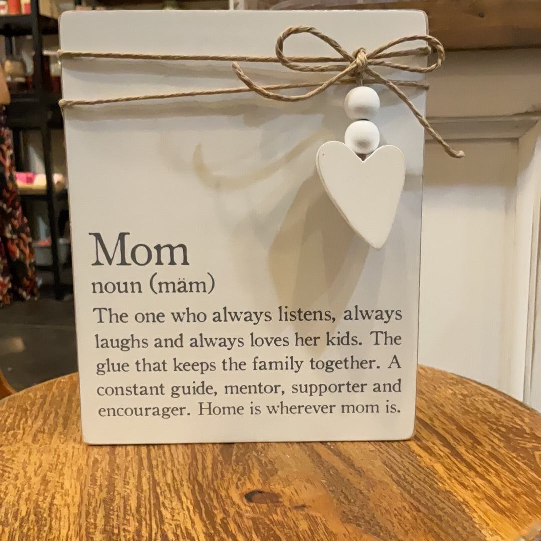 White definition plaques with twine wrapped around with a heart attached featuring "Mom". Displays "The who always listens, always laughs and always loves her kids. The glue that keeps the family together. A constant guide, mentor, supporter and encourager. Home is wherever mom is."