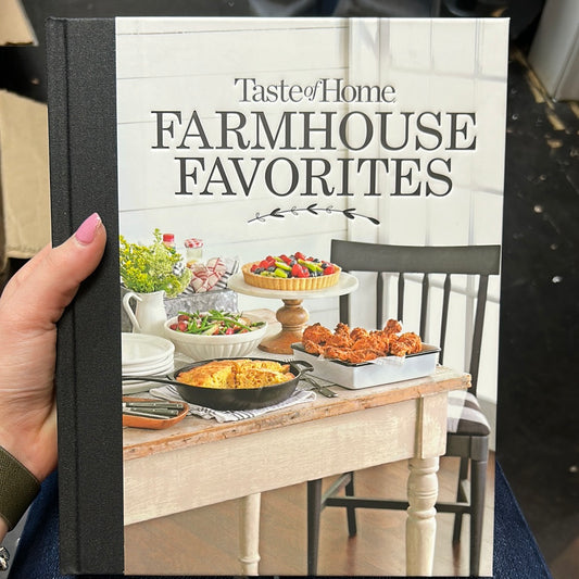 Book with black binding featuring a farmhouse kitchen scene with "Taste of Home: Farmhouse Favorties" in black lettering.
