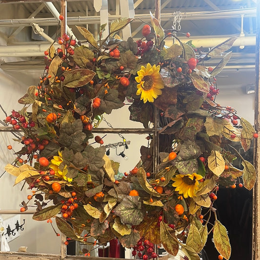 Fall wreath with green leaves, yellow sunflowers, red berries and small orange pumpkins.