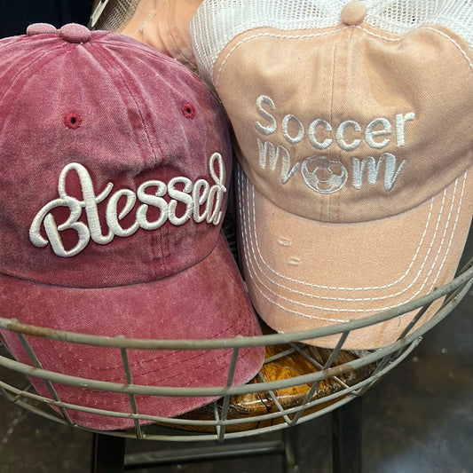 Red women's hat featuring "Blessed". Pink women's hat featuring "soccer mom".