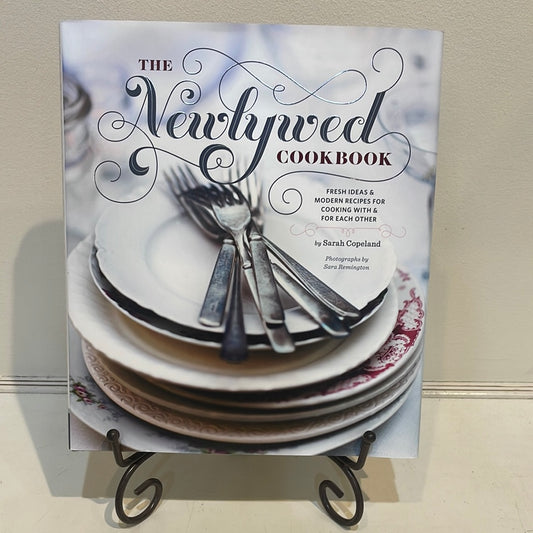 Book with silverware and plates titling "The Newlywed Cookbook".