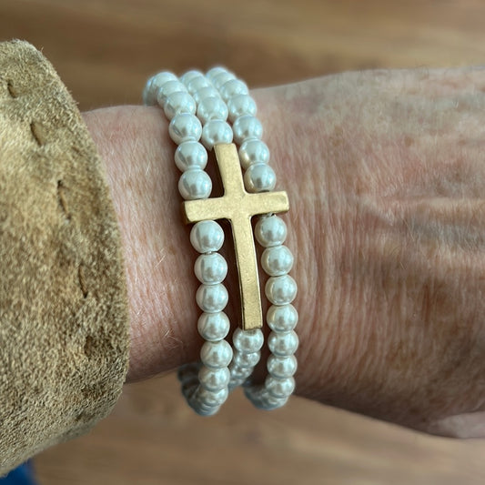 Pearl colored beaded bracelet stack with golden cross.