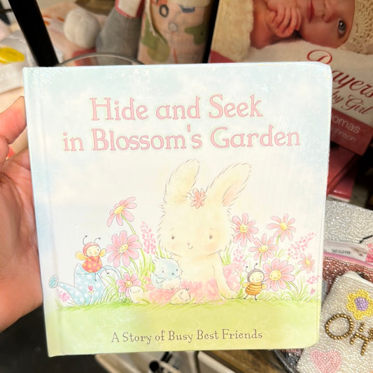 A book featuring a garden with a white bunny and pink flowers, titling "Hide and Seek in Blossom's Garden: A Story of Busy Best Friends".