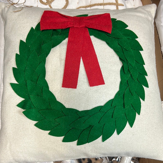 Off-white pillow with a green felt crafted wreath, with a red felt bow.