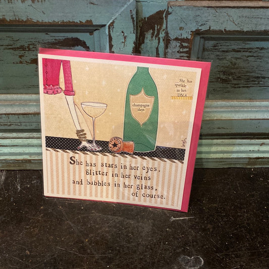 Card with the bottom half of a woman holding her champagne glass next to a champagne bottle. Says "She has stars in her eyes, glitter in her veins and bubbles in her glass, of course."