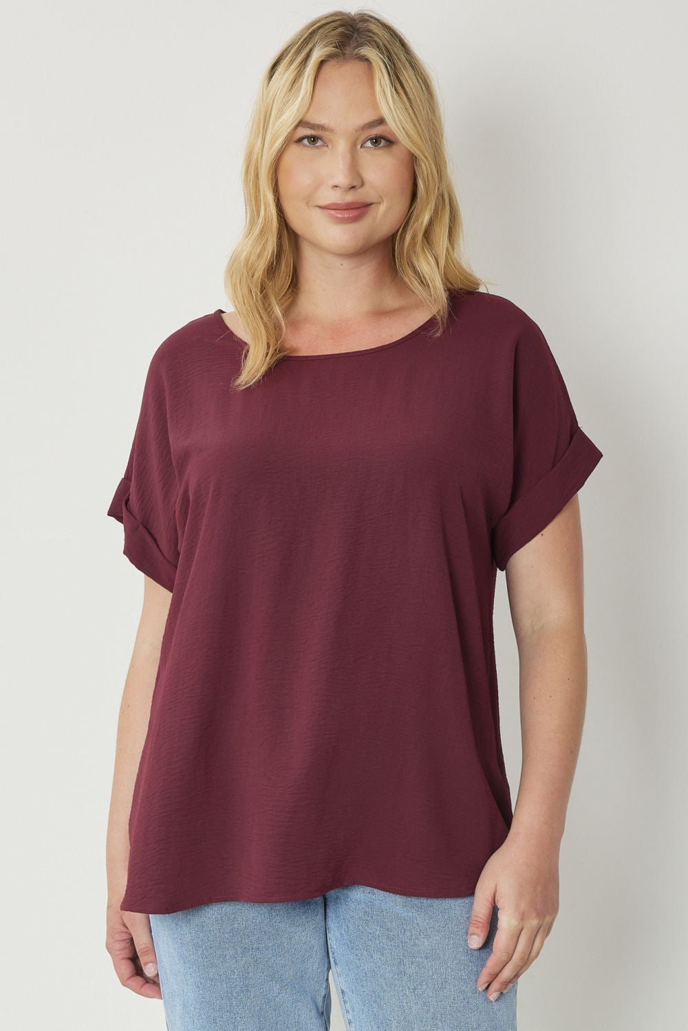 Burgundy scoop-neck top featuring permanent rolled sleeve detail and an asymmetrical hem.