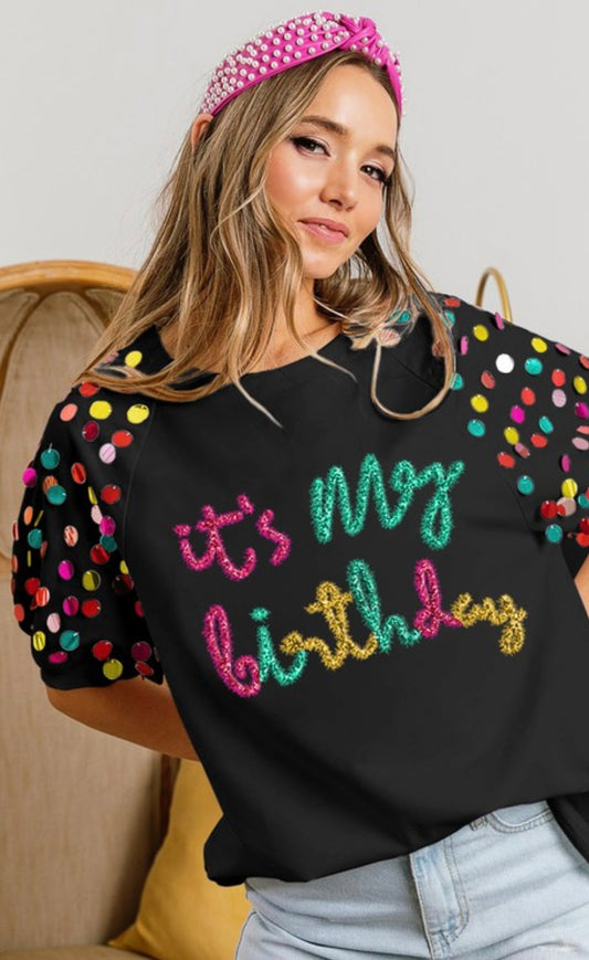 Model featuring black half sleeve top with sequins with "IT's my birthday" in pink, green, and gold.