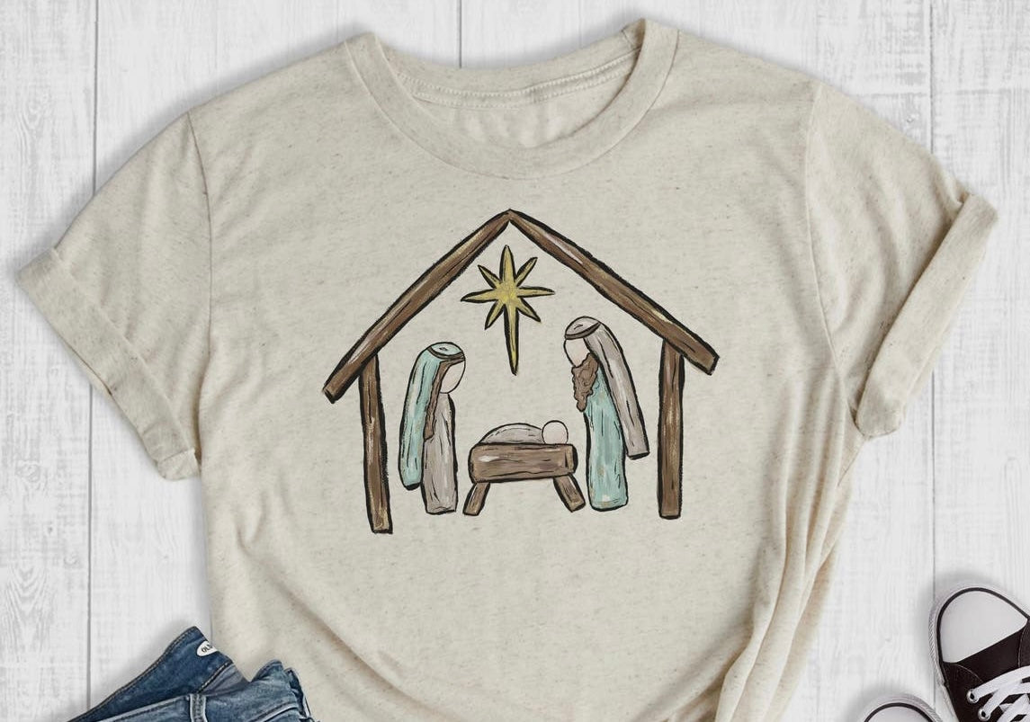 Cream Christmas Graphic T-Shirt featuring a nativity scene.