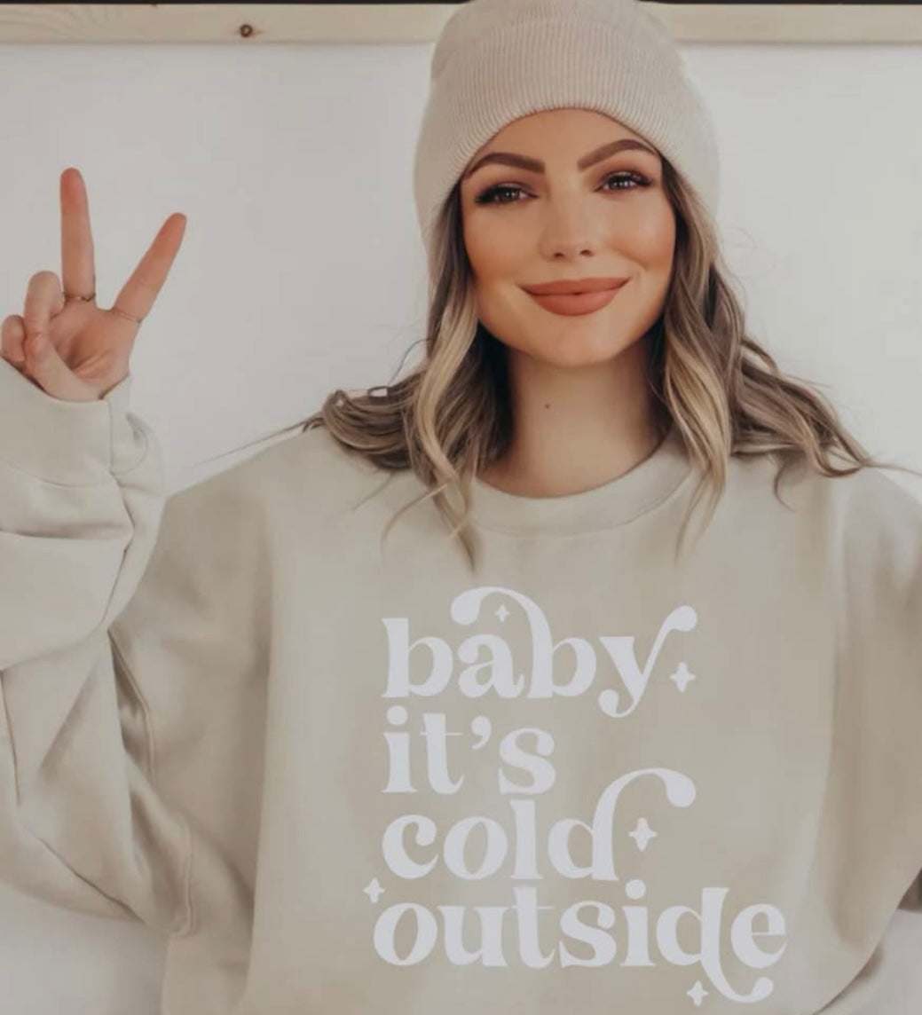 Model featuring a cream colored sweatshirt displaying "Baby, it's cold outside" in white lettering.