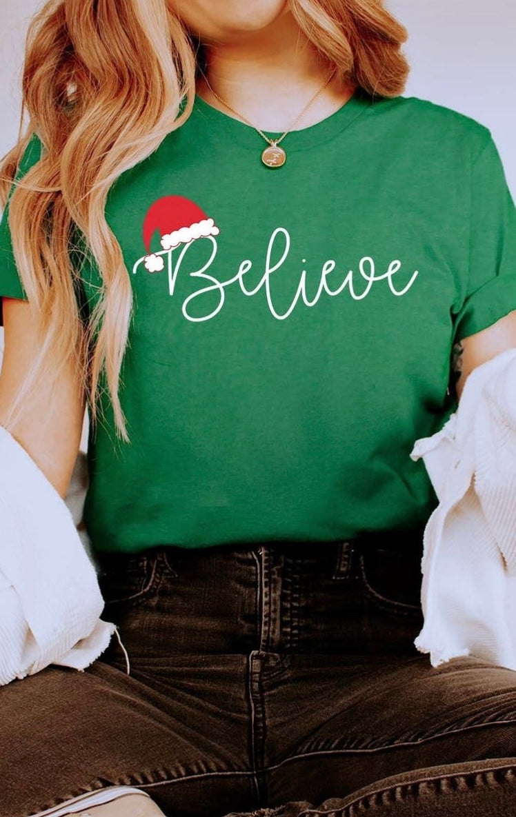 Green Christmas Graphic T-Shirt featuring "Believe" in white lettering with a Santa hat.