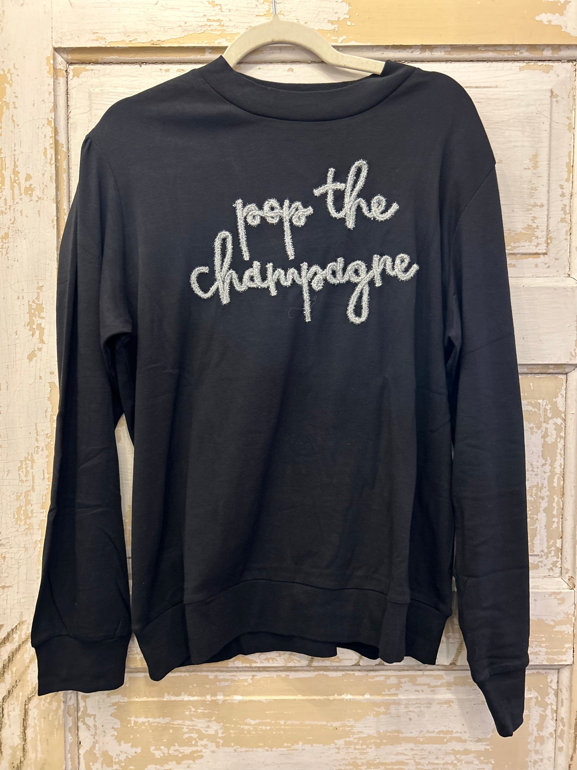 Black long sleeve top featuring "Pop the champagne" in glitter stitching.