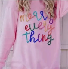 Model featuring pink "Merry Everything" sweater with colorful stitching.