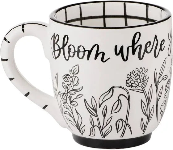 White handmade mug with a black outline of flowers featuring "Bloom where you're planted".