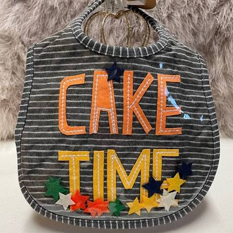 Black and white striped bib with "CAKE" in orange and "TIME" in yellow with multicolored stars on the bottom.