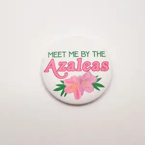 Golf button with an azalea featuring "Meet me by the azaleas" in green and pink lettering.