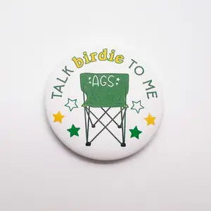 Golf button featuring a foldable green chair with "Talk birdie to me" in green and yellow lettering.