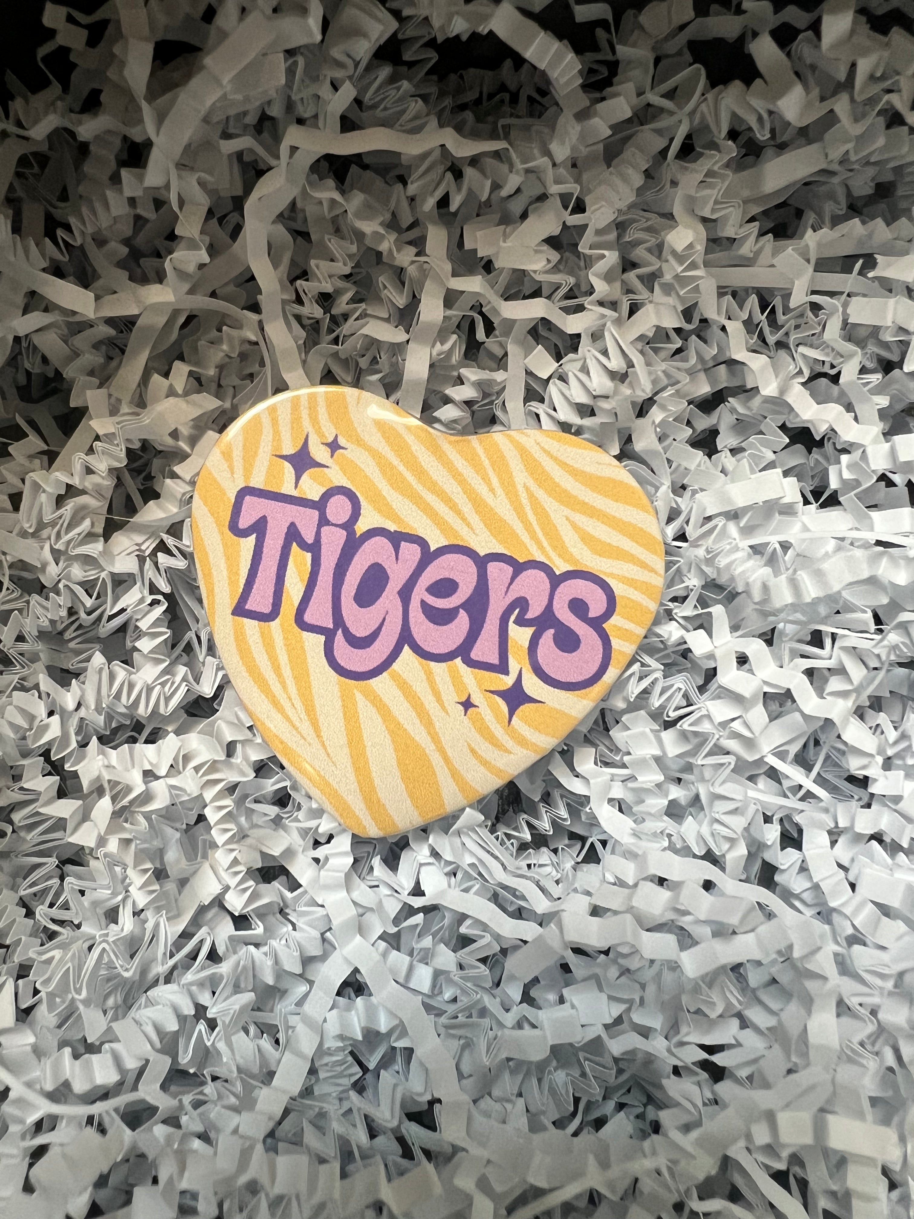LSU button with gold tiger stripe background featuring "Tigers" in purple lettering.