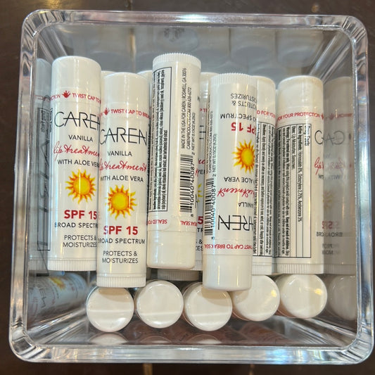 Tubes of Caren vanilla lip treatment with aloe vera in white packaging with black and red lettering with a sun. SPF 15.